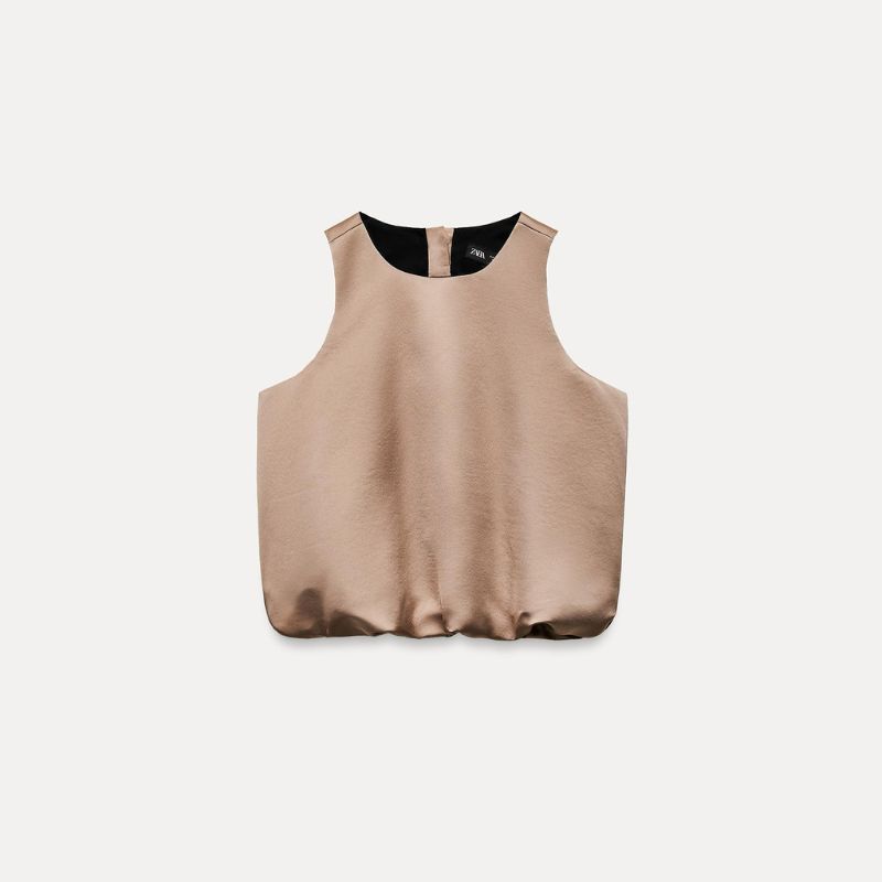 tendencia blusas 2000 en 2025 CUERPO SATINADO GLOBO color Visón Cuerpo de cuello redondo y manga sisa. Bajo abullonado acabado en elástico. Cierre en espalda con botón dorado.